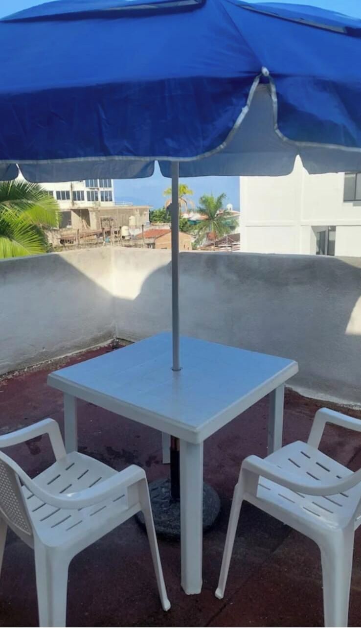 Eine Dachterrasse mit Tisch und zwei Stühlen unter einem blauen Sonnenschirm.