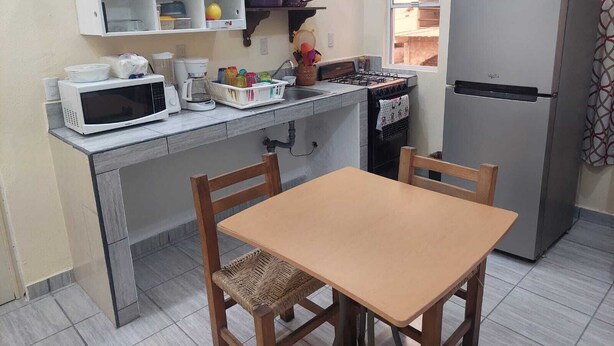 A compact kitchen with a microwave, coffee maker, and a refrigerator. There is a wooden table and chairs, and a window providing natural light.