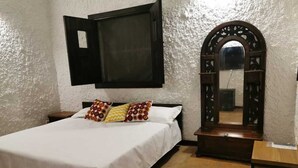 A bedroom with a bed, a TV mounted on the wall, a wooden dresser, and a mirror with an ornate frame. - Cabaña Colonia Española (Risaralda)