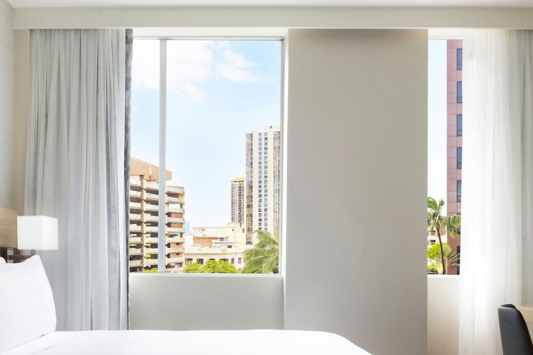 A hotel room with a large window, a bed, a nightstand, and a lamp.