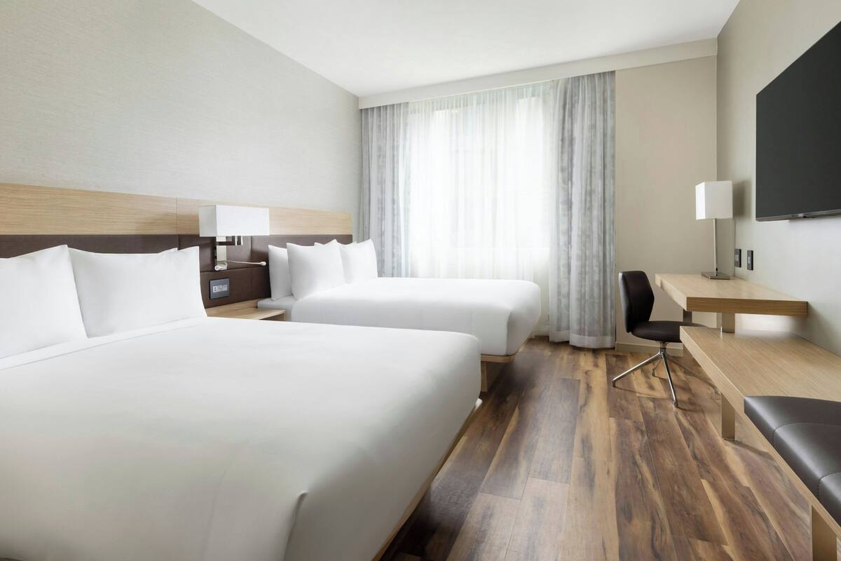 A hotel room with two beds, a desk, a chair, and a TV.