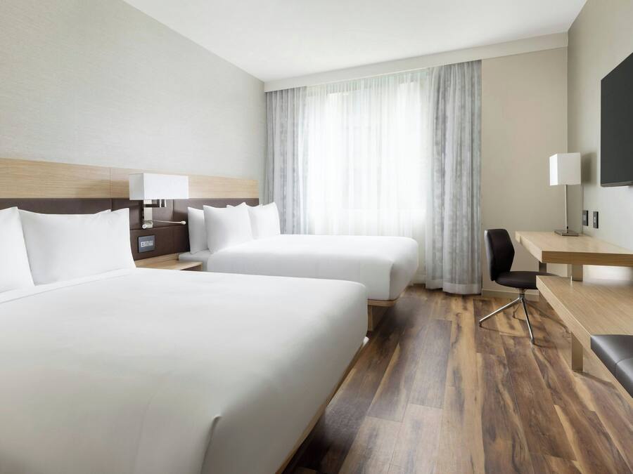 A hotel room with two beds, a desk, a chair, and a TV.