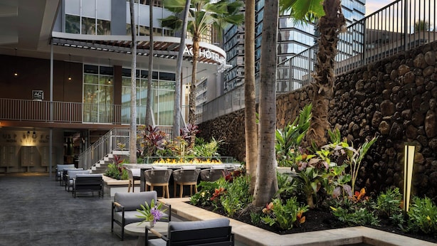 A hotel lobby with outdoor seating, a stone wall, and a fire feature. - AC Hotel by Marriott Honolulu (Honolulu)