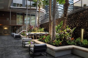 A hotel lobby with outdoor seating, a stone wall, and a fire feature. - AC Hotel by Marriott Honolulu (Honolulu)