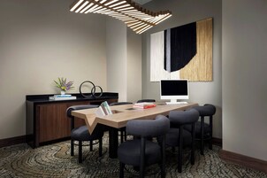 Une salle de réunion moderne équipée d’une longue table, de six chaises, d’un écran d’ordinateur et d’un élément décoratif mural.
