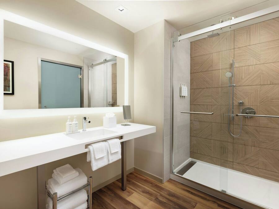 A modern bathroom with a large mirror, white sink, and a glass-enclosed shower.
