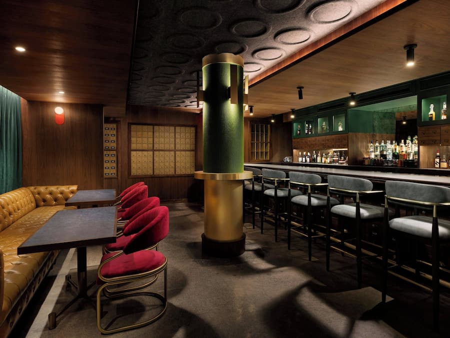 A bar area with a high bar counter, multiple stools, a cushioned bench, and a unique cylindrical column.