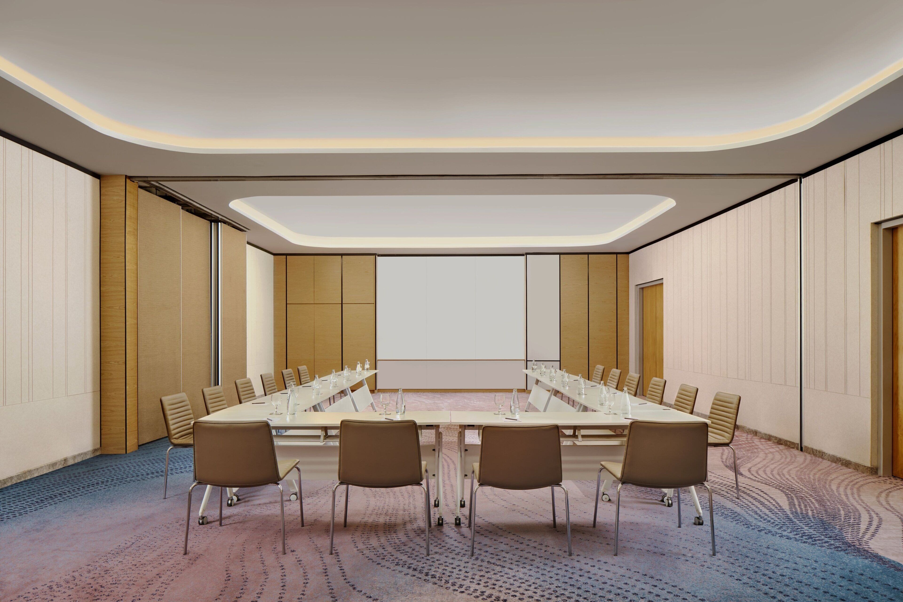 A conference room with a long table, chairs, and a large screen.
