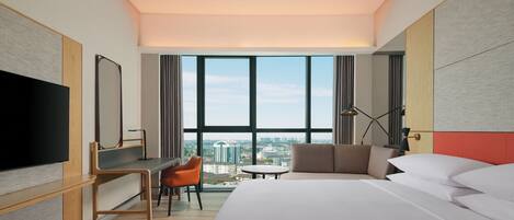 Een moderne hotelkamer met een groot bed, een bureau, een stoel, een televisie en uitzicht op de stad door grote ramen.