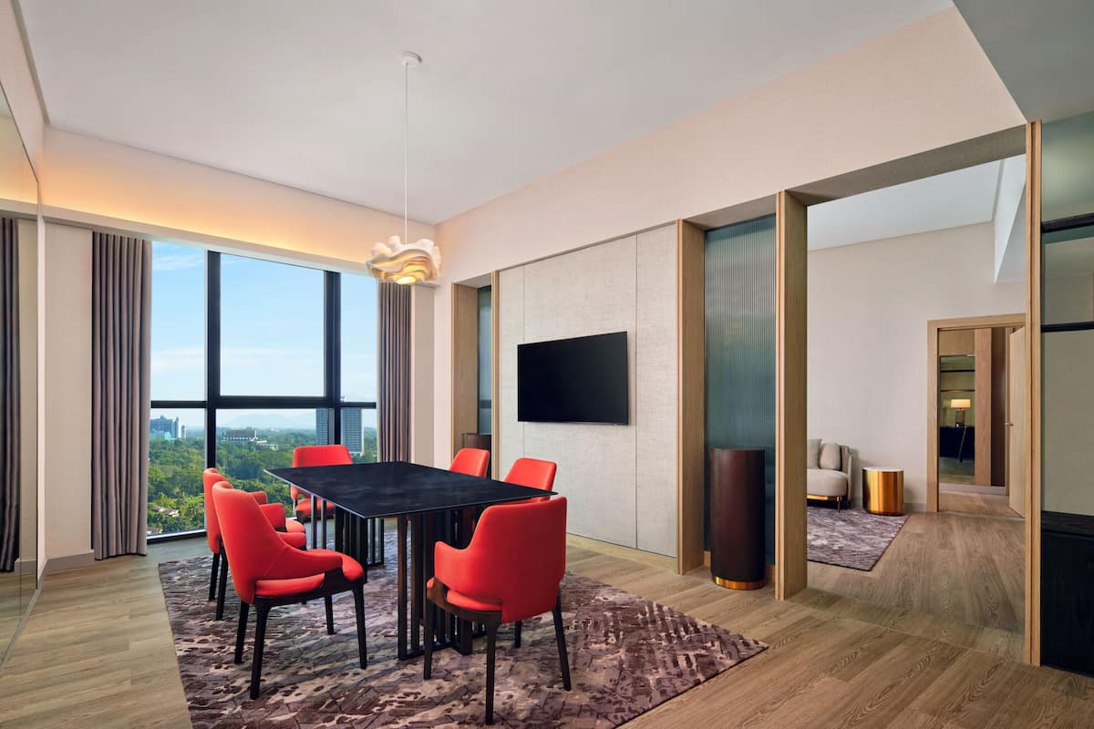 A modern conference room with a large table, red chairs, a flat-screen TV, and a city view through large windows.