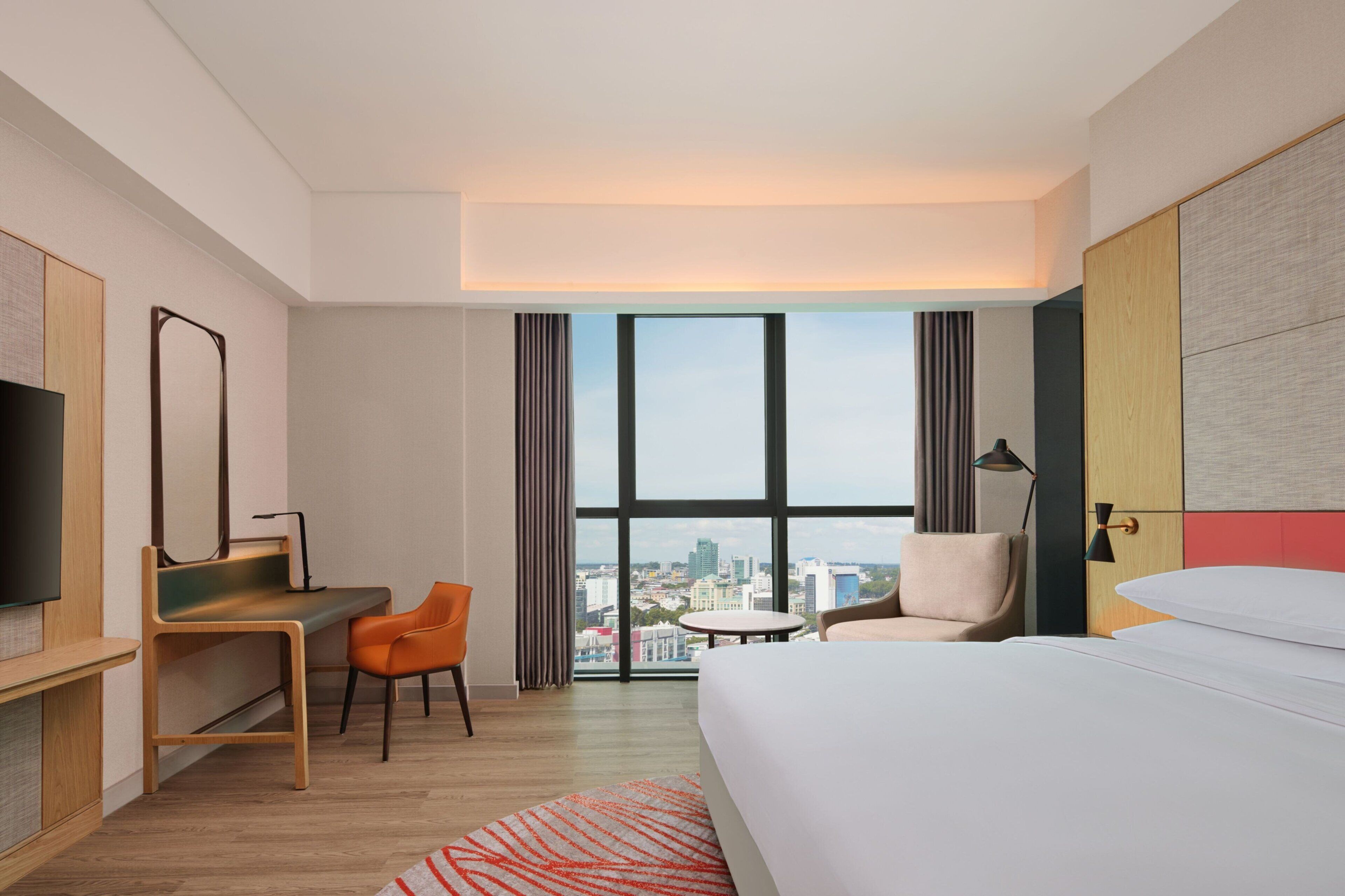 A hotel room with a large window, a bed, a desk, and a chair.