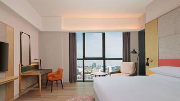 A hotel room with a large window, a bed, a desk, and a chair.