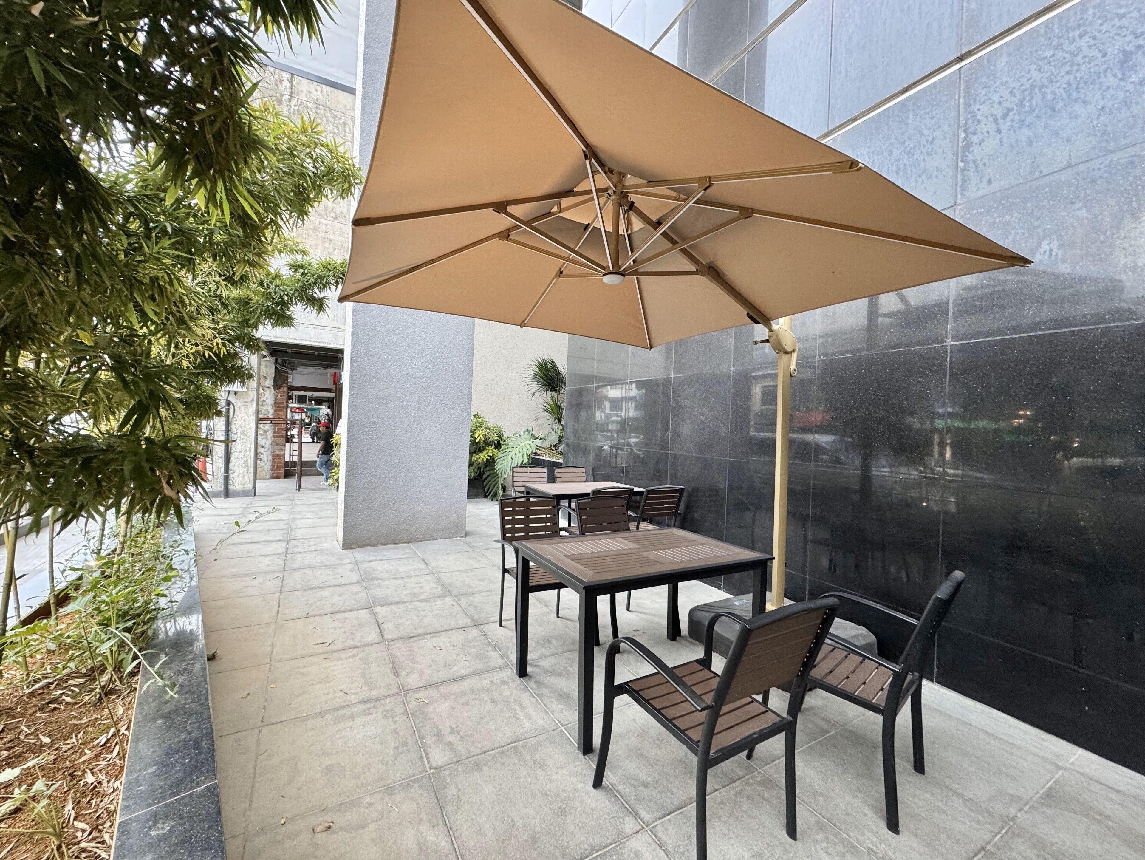 An outdoor patio area with a table and chairs under a large umbrella, surrounded by a stone wall and greenery.