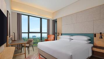 Habitación de hotel moderna con una cama grande, un escritorio, una silla y vistas de la ciudad a través de amplios ventanales.