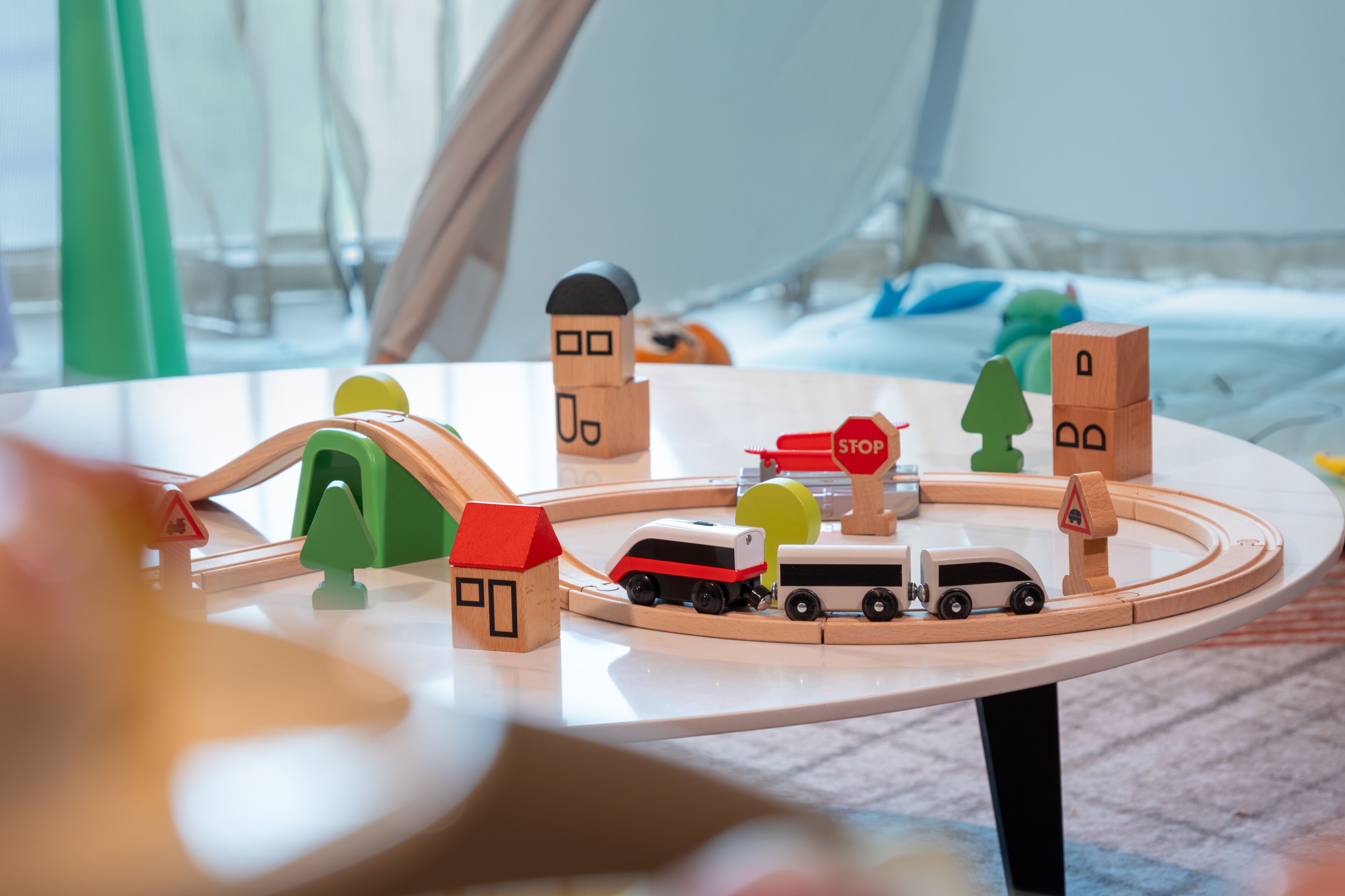A wooden toy train set on a table with a house, a stop sign, and a bus.