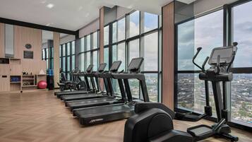 Un gimnasio con varias cintas de correr y equipo de ejercicio, ventanas amplias y vista panorámica de la ciudad.