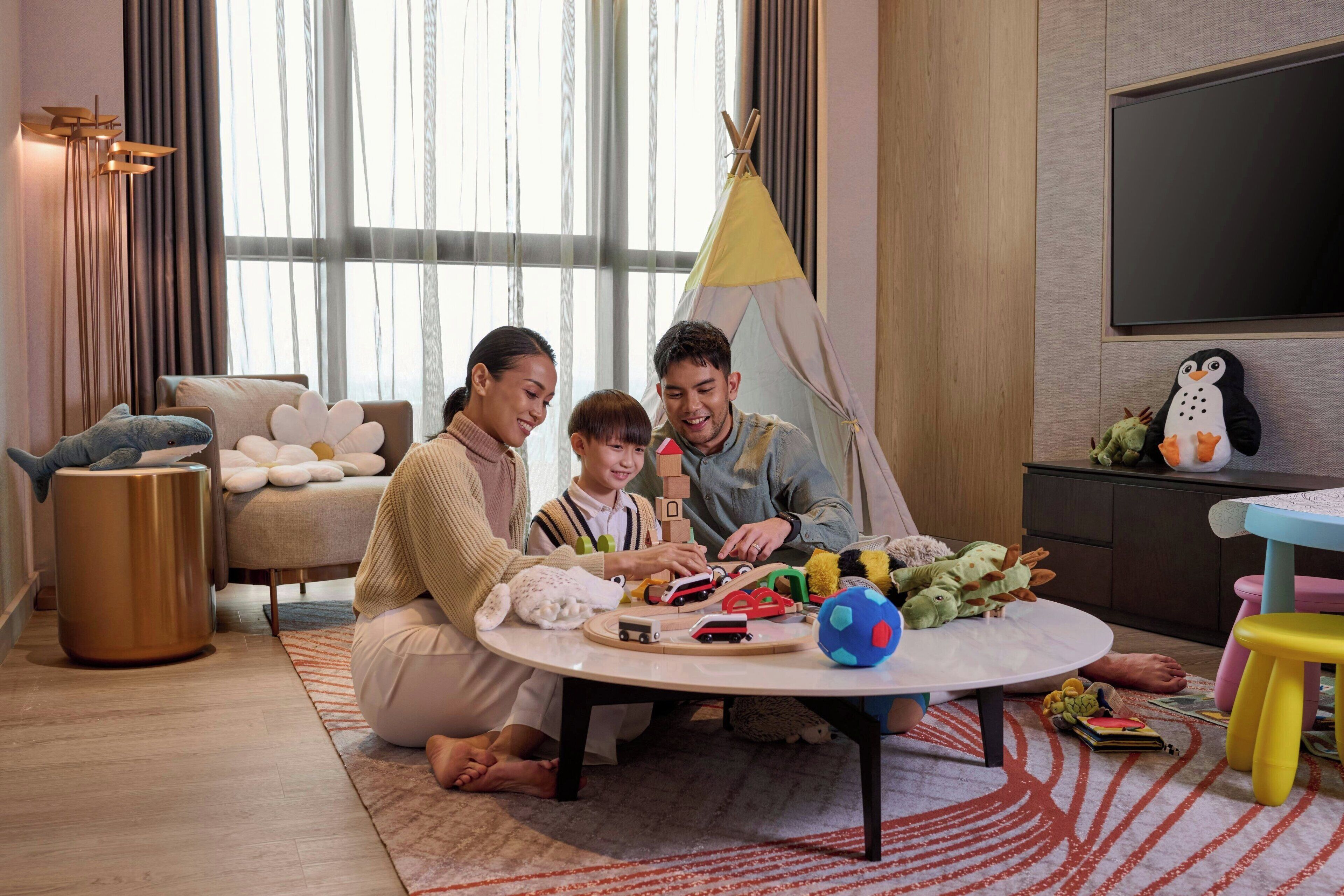 A family playing with toys in a modern living room with a large window, a flat-screen TV, and a cozy seating area.