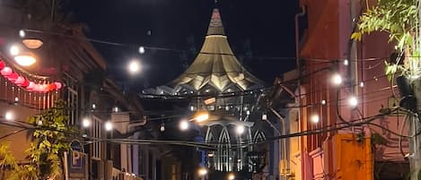 A street at night with a prominent building featuring a pointed roof and illuminated by string lights.