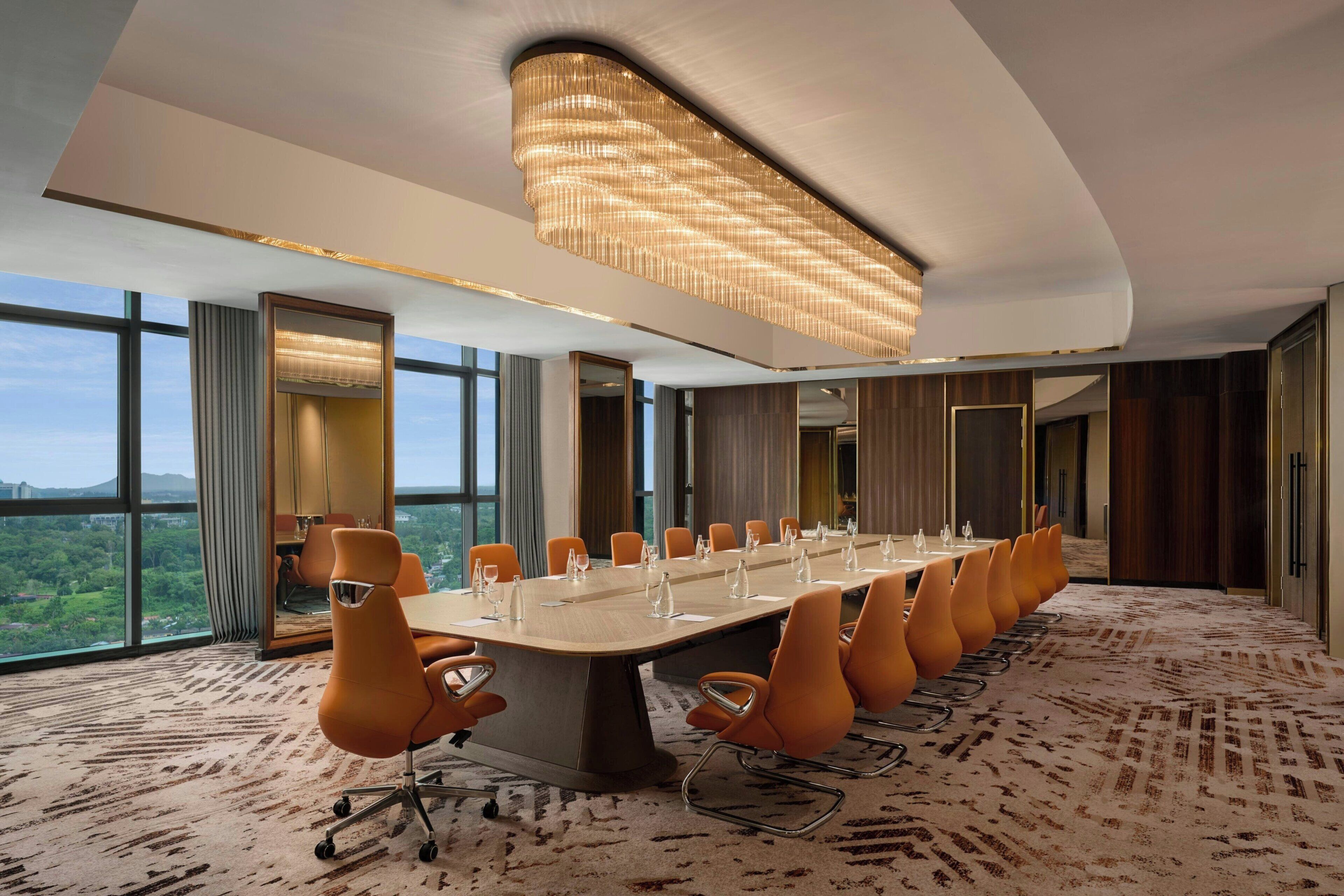 A conference room with a long table, orange chairs, and a large chandelier.