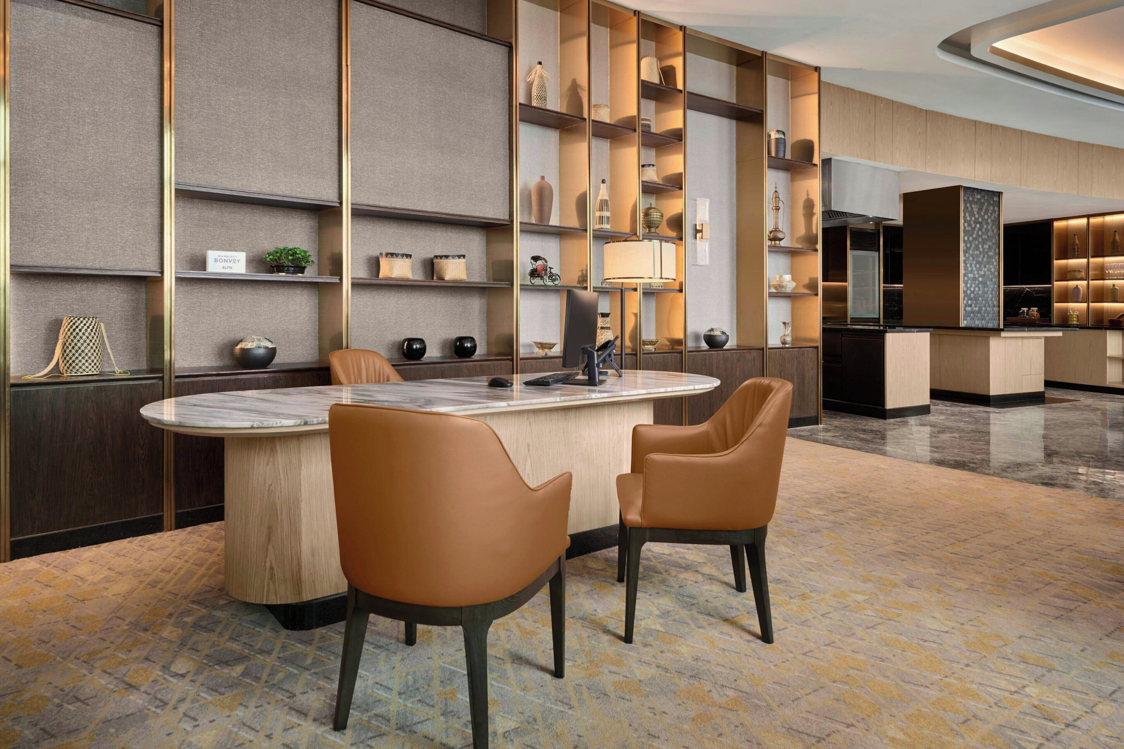 A modern hotel lobby with a marble reception desk, leather chairs, and a patterned carpet.