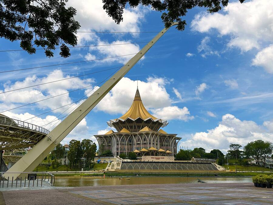 A large, modern building with a distinctive golden roof and a bridge in the foreground.