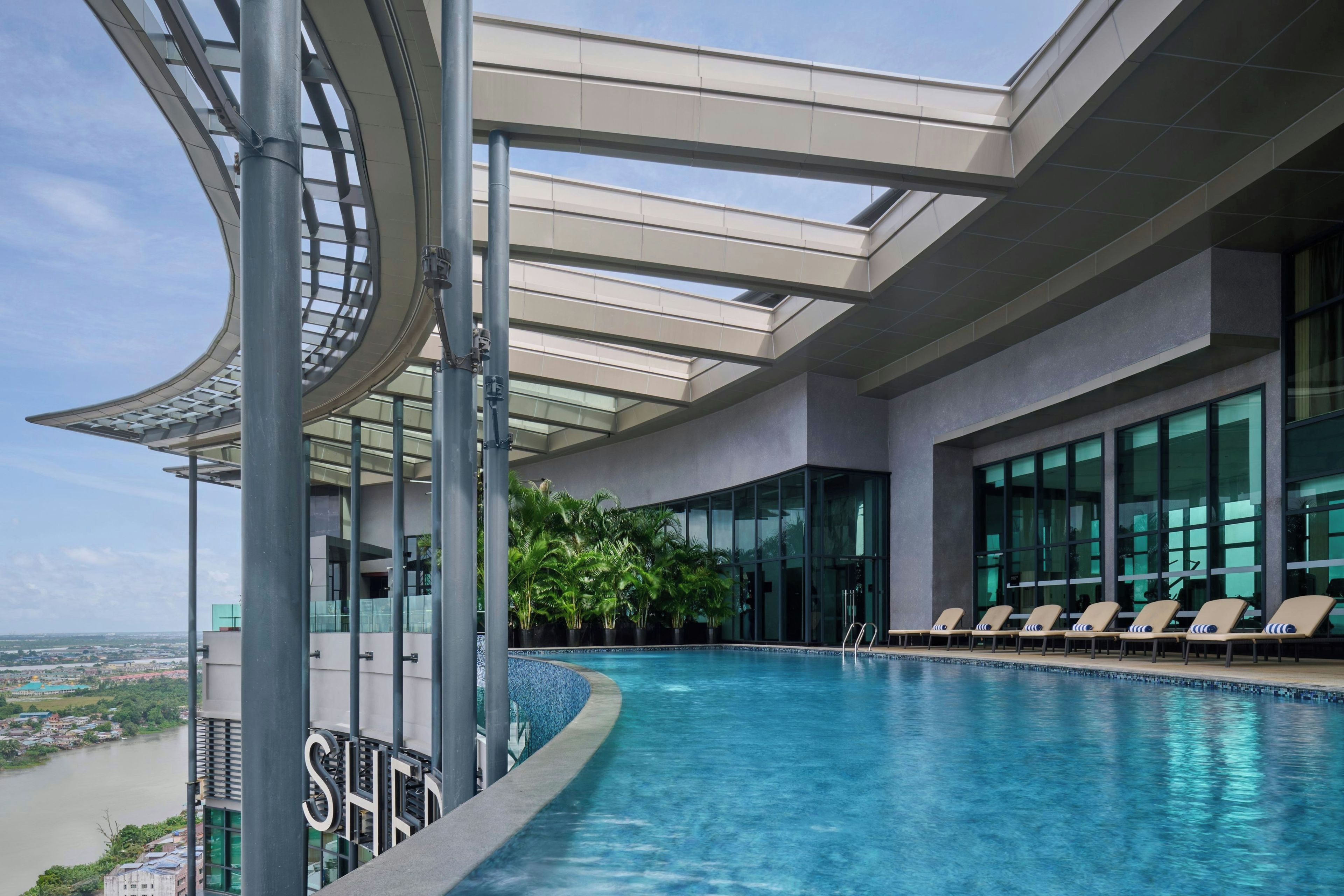 An indoor infinity pool with lounge chairs, a glass balustrade, and a view of a river.
