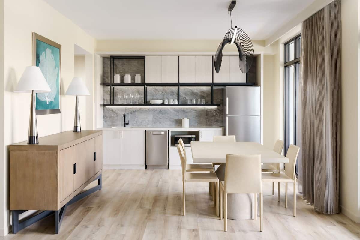 Une cuisine moderne avec un coin repas, comprenant un plan de travail en marbre, des appareils en acier inoxydable et une table à manger en bois avec des chaises.