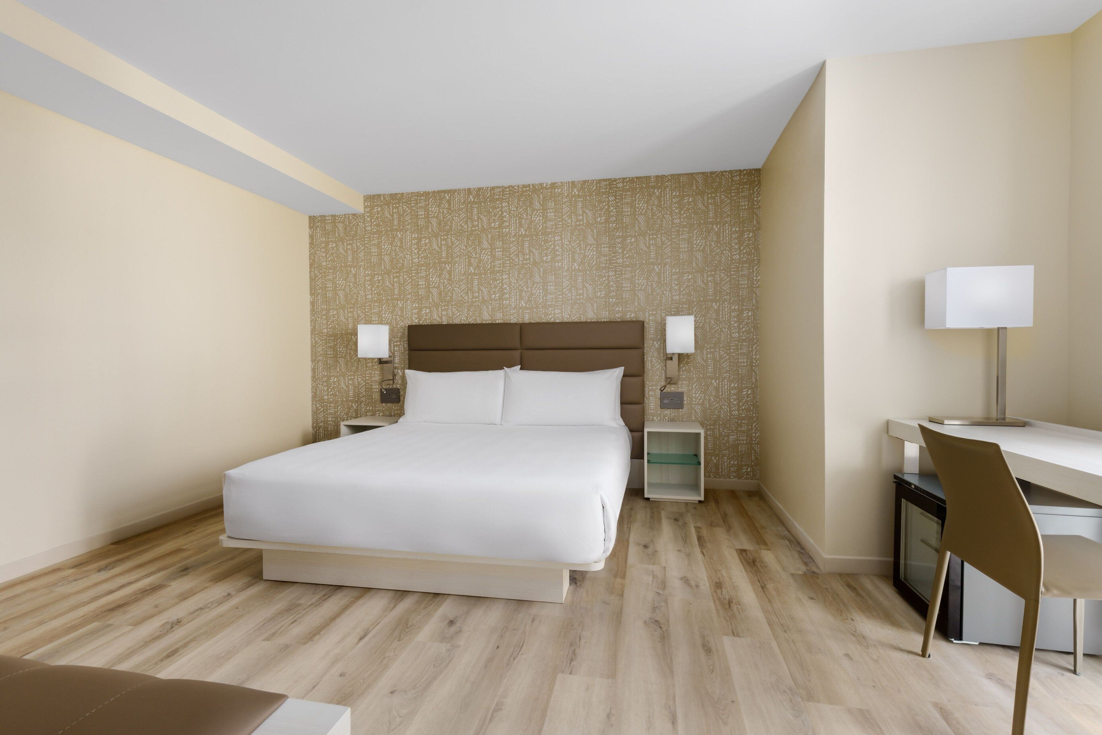 Una habitación de hotel con una cama grande, mesitas de noche, un escritorio y una silla.
