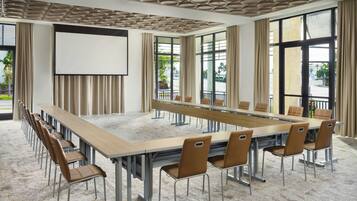 A conference room with a long table, chairs, a projector screen, and large windows with curtains.