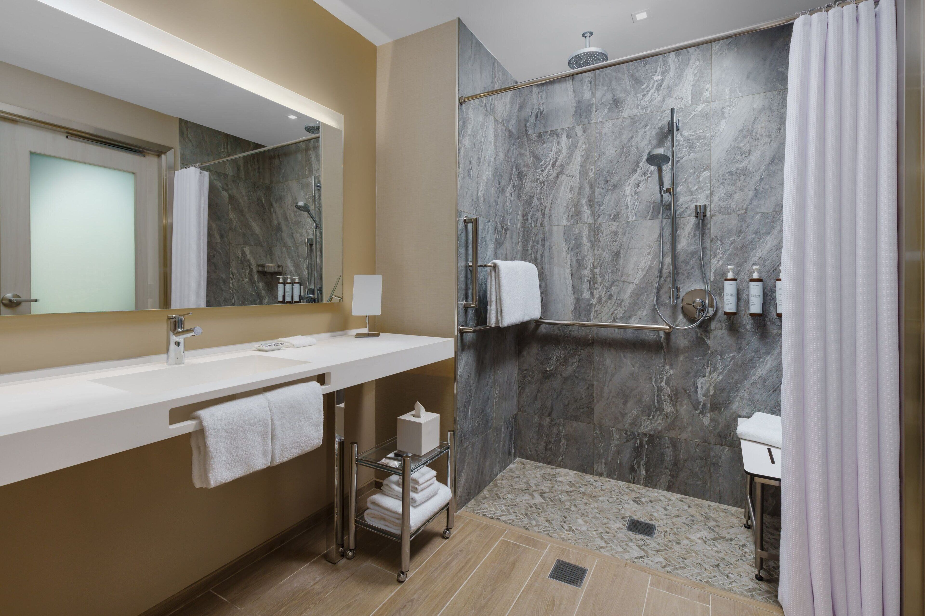 Un bagno moderno con doccia in marmo, lavandino bianco e porta asciugamani in vetro.