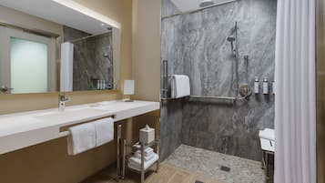 Un bagno moderno con doccia in marmo, lavandino bianco e porta asciugamani in vetro.