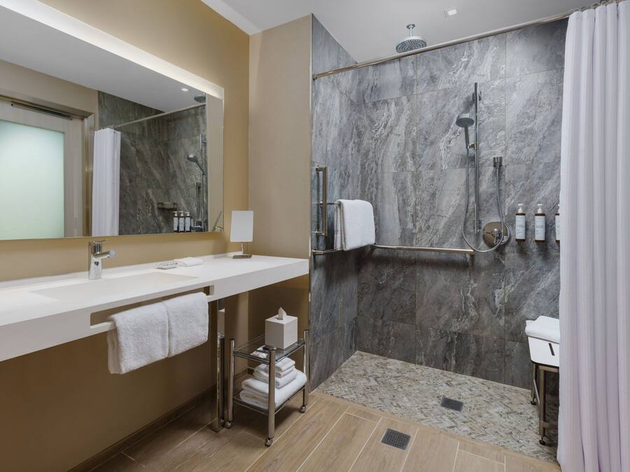 Un bagno moderno con doccia in marmo, lavandino bianco e porta asciugamani in vetro.