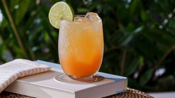 A glass of orange beverage with a lime slice on a coaster, placed on a book with a woven mat underneath.