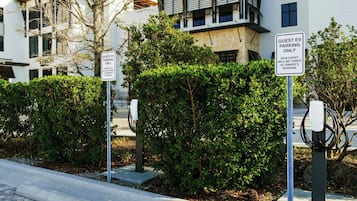 Un edificio moderno con señalización para estacionamiento de vehículos eléctricos para huéspedes y una estación de carga.