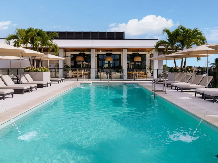 Ein Poolbereich mit Liegestühlen und Sonnenschirmen, ein Schwimmbecken und ein Gebäude mit großen Fenstern und einem Balkon.