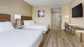 Quarto de hotel com duas camas, uma escrivaninha, uma cadeira, uma televisão e uma porta para o banheiro.