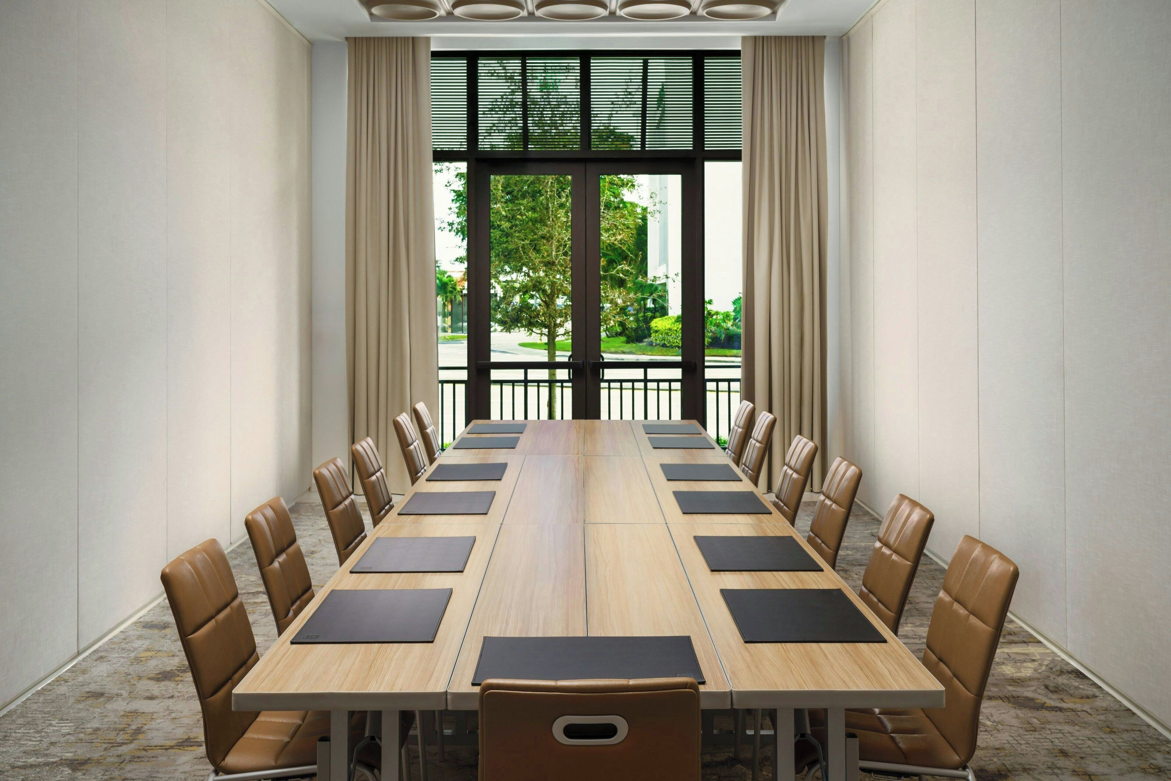 A conference room with a long table, brown leather chairs, and a view through large windows.