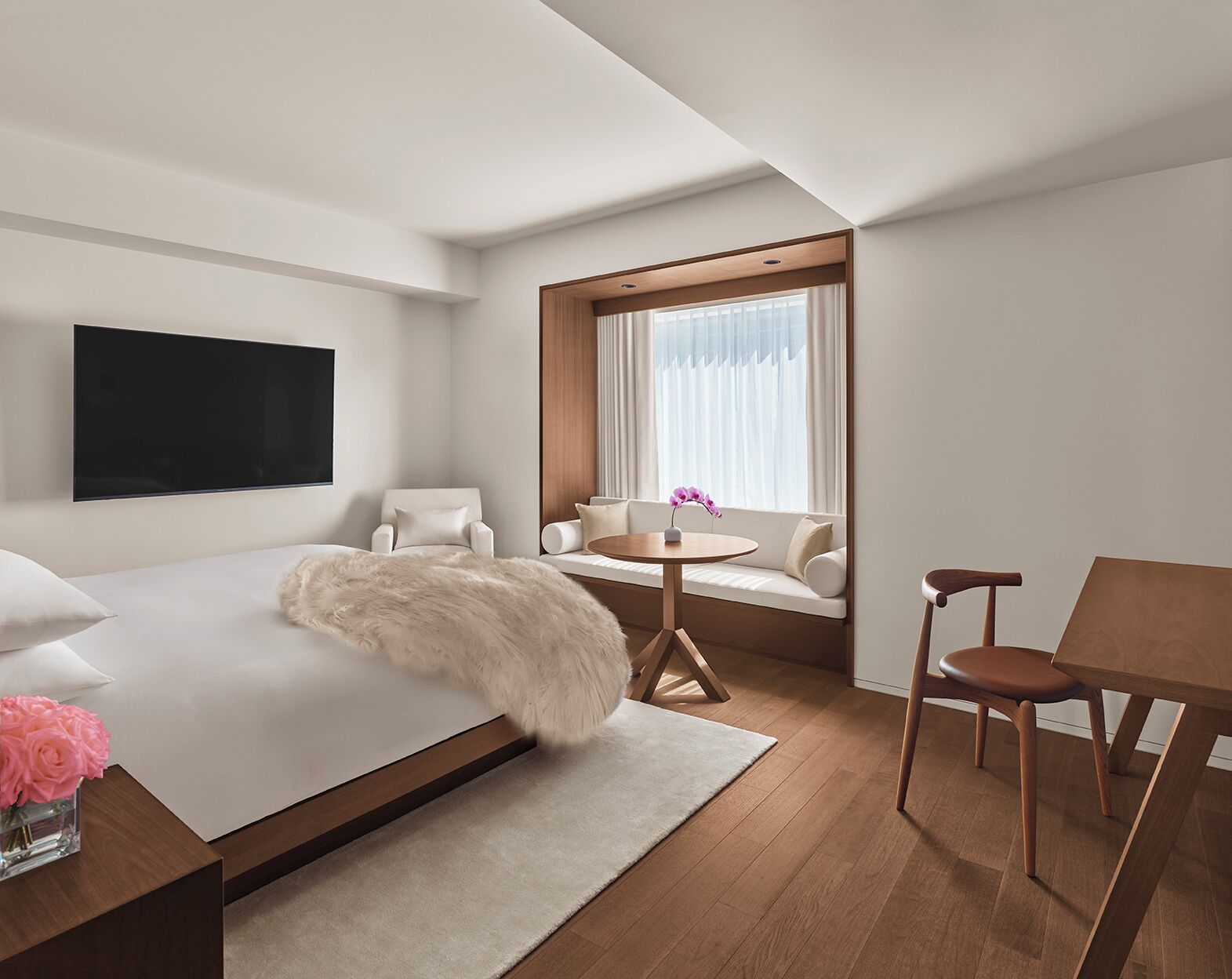 Una habitación de hotel moderna con una cama grande, un televisor montado en la pared, un sofá con una mesita y una ventana con cortinas.