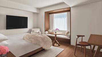 Una habitación de hotel moderna con una cama grande, un televisor montado en la pared, un sofá con una mesita y una ventana con cortinas.