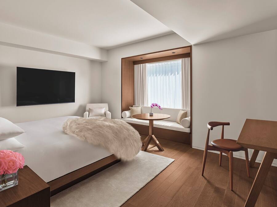 Una habitación de hotel moderna con una cama grande, un televisor montado en la pared, un sofá con una mesita y una ventana con cortinas.