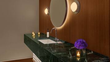 Une salle de bain moderne avec un lavabo en marbre, un meuble-lavabo en bois et un grand miroir doté d’un éclairage intégré.