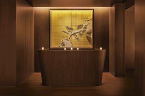 A reception area with a wooden reception desk, a large framed artwork depicting a tree, and three lit candles on the desk.