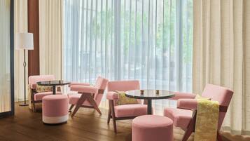 A modern room with pink upholstered chairs and ottomans, a round table, and a floor lamp.