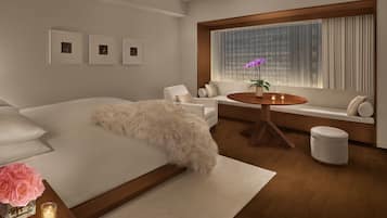 Quarto moderno com uma cama grande, um sofá, uma mesa de madeira redonda e uma janela com cortinas.