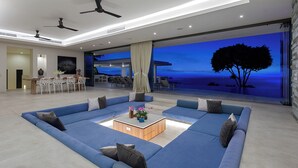 A modern living room with a large sectional sofa, a coffee table, and a view of the ocean at dusk. - Villa Spice (Koh Samui)