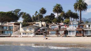A beachfront property with multiple-story houses, a sandy beach, and palm trees. - Oceanfront Cottage on the Sand at Miramar Beach (Santa Barbara)