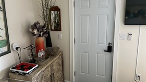 A hallway with a white door, a small console table with decorative items, a vase, and a wall-mounted television.