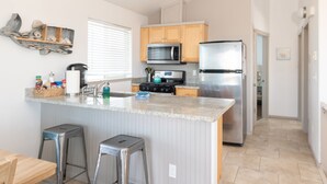 A modern kitchen with a central island, stainless steel appliances, wooden cabinets, and a window with blinds. - Dog-Friendly Beach Escape - 20% off March stays (Moclips)