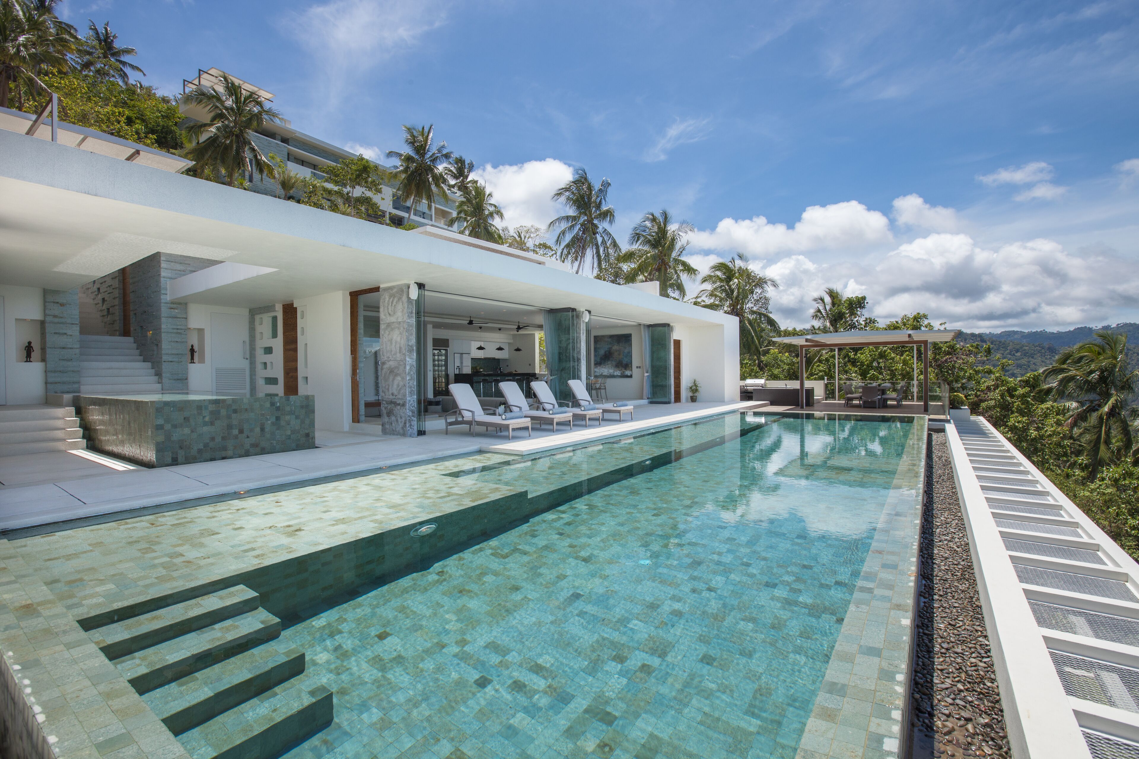 A modern poolside area with a clear pool, lounge chairs, and a covered seating area.