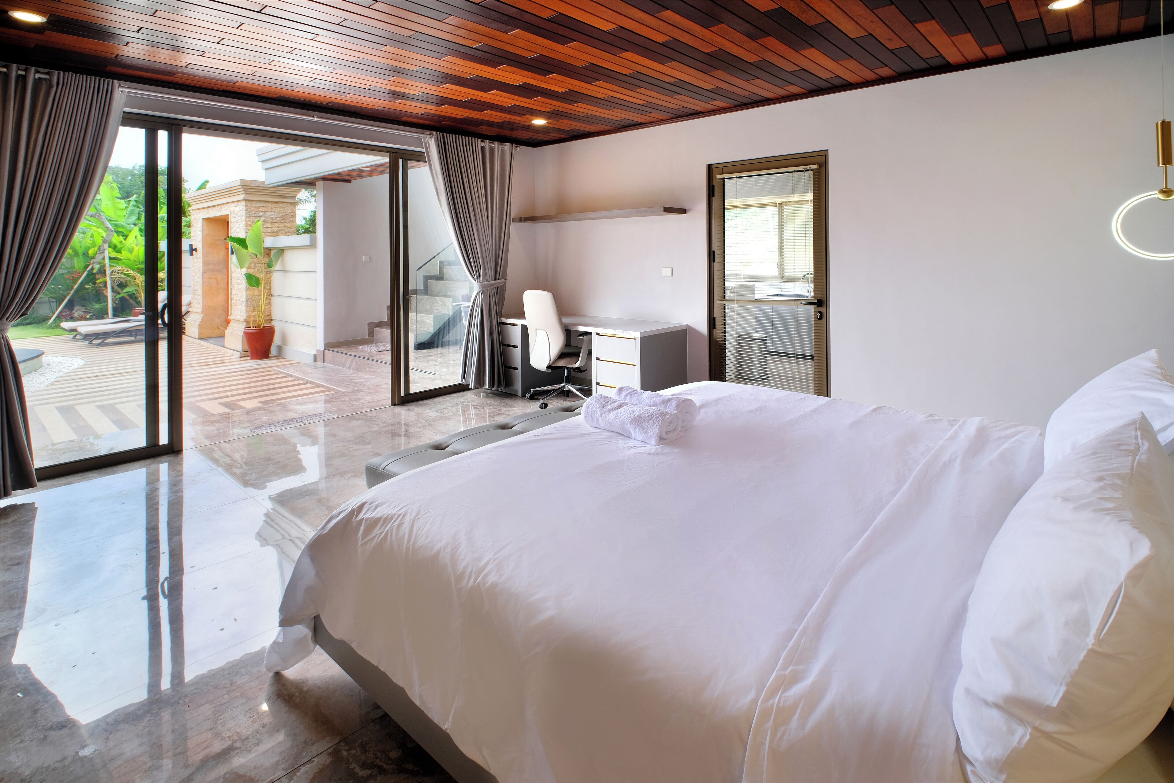 A modern bedroom with a large bed, a desk, and a sliding glass door leading to a balcony.